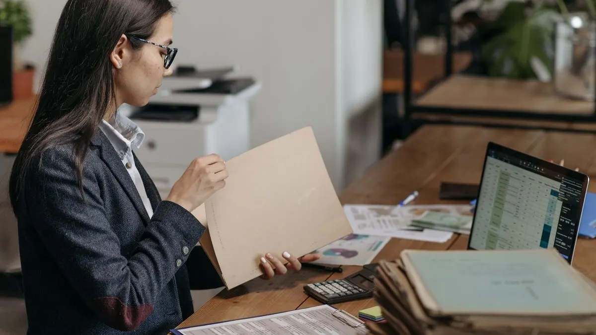 Persona revisando documentación en una oficina con un portátil y carpetas sobre la mesa