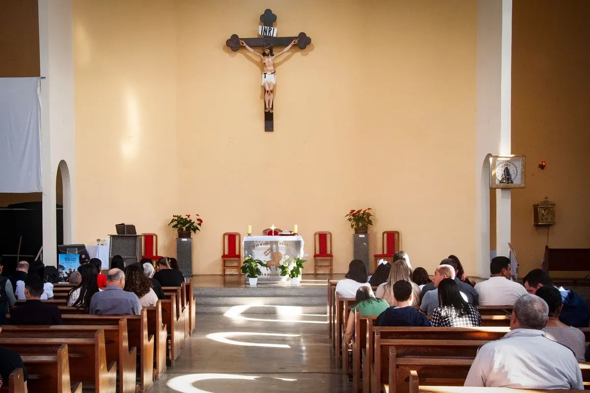 O congregație în băncile unei biserici creștine, în fața altarului și a unui crucifix.