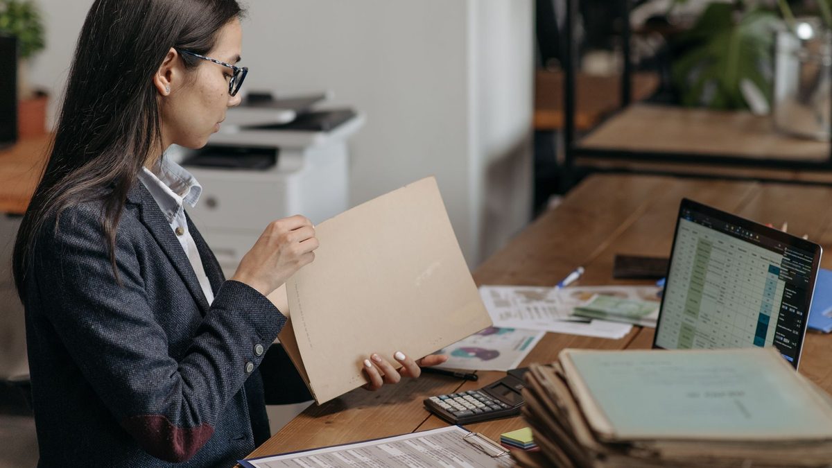 Persona revisando documentación en una oficina con un portátil y carpetas sobre la mesa