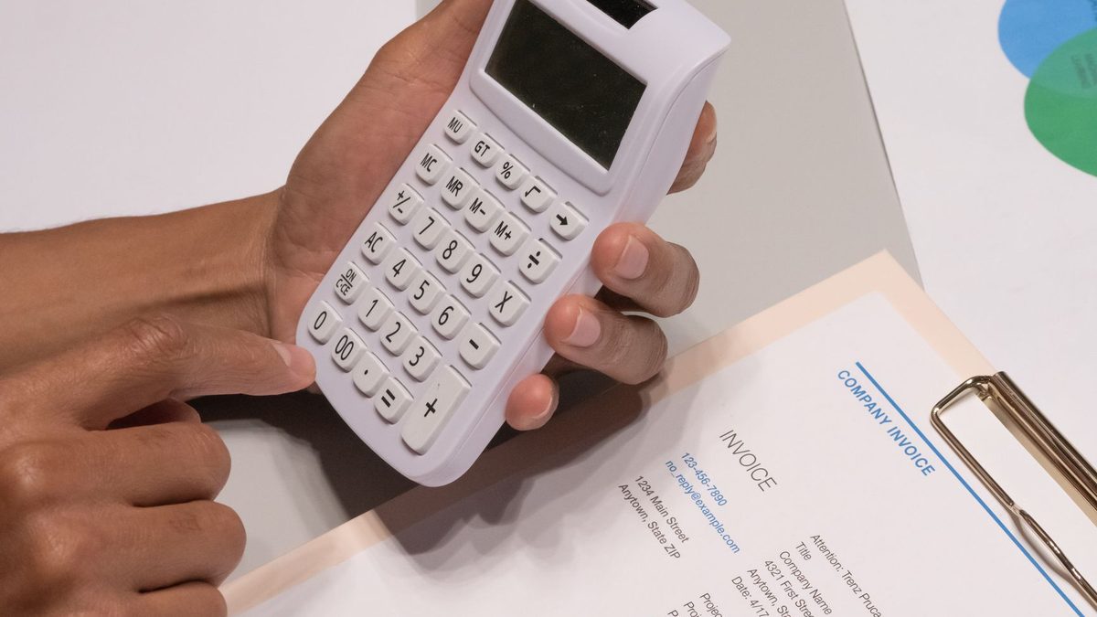 Manos usando una calculadora junto a una factura de empresa para calcular el presupuesto de un proyecto